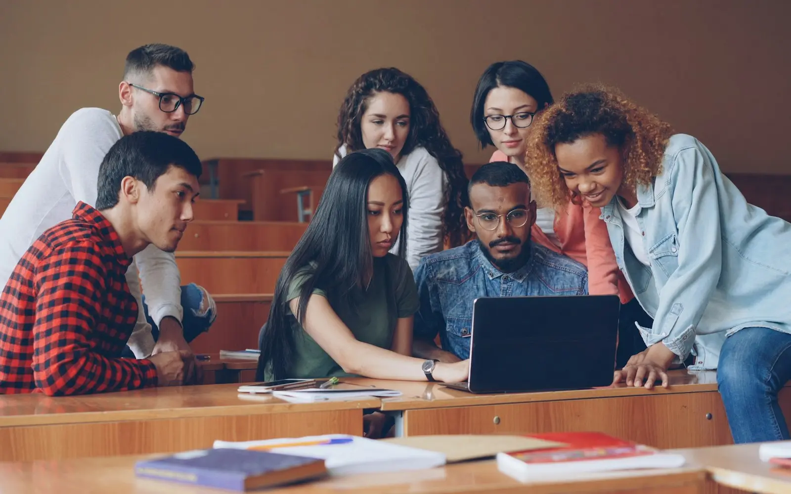 Group of students gathered around a laptop in a lecture hall